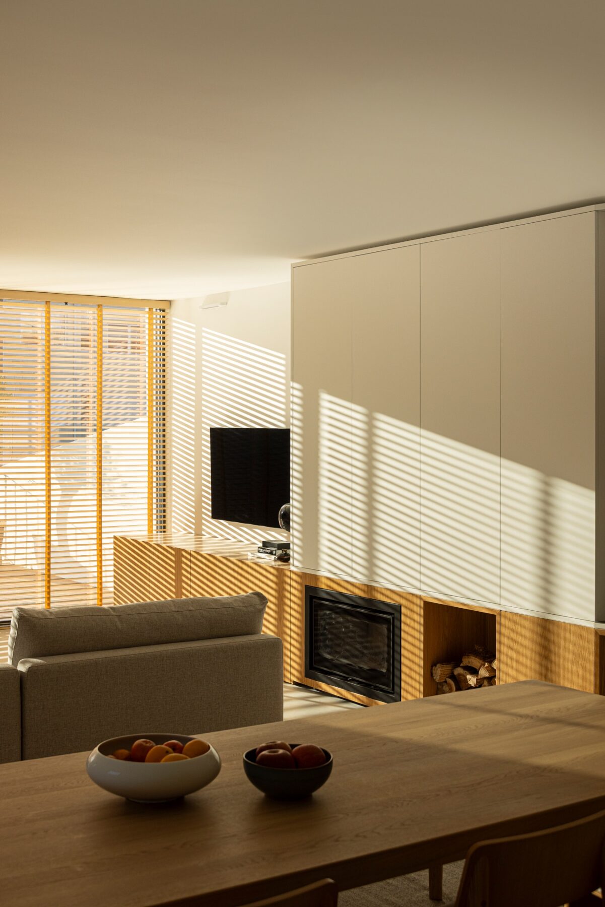 Sala de estar com luz natural filtrada por estores de madeira, sofá e mesa de jantar — Casa sem Rua