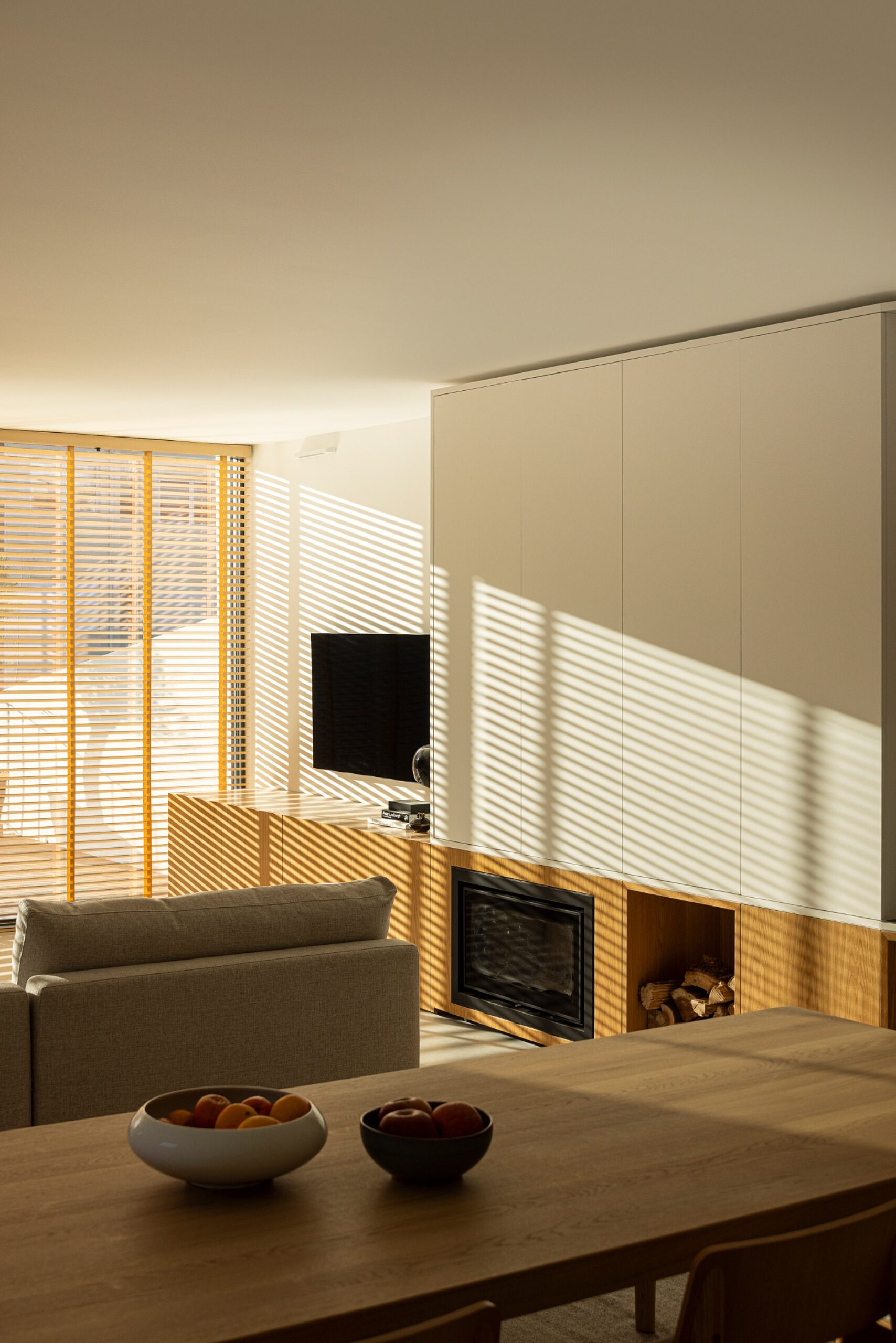 Sala de estar com luz natural filtrada por estores de madeira, sofá e mesa de jantar — Casa sem Rua