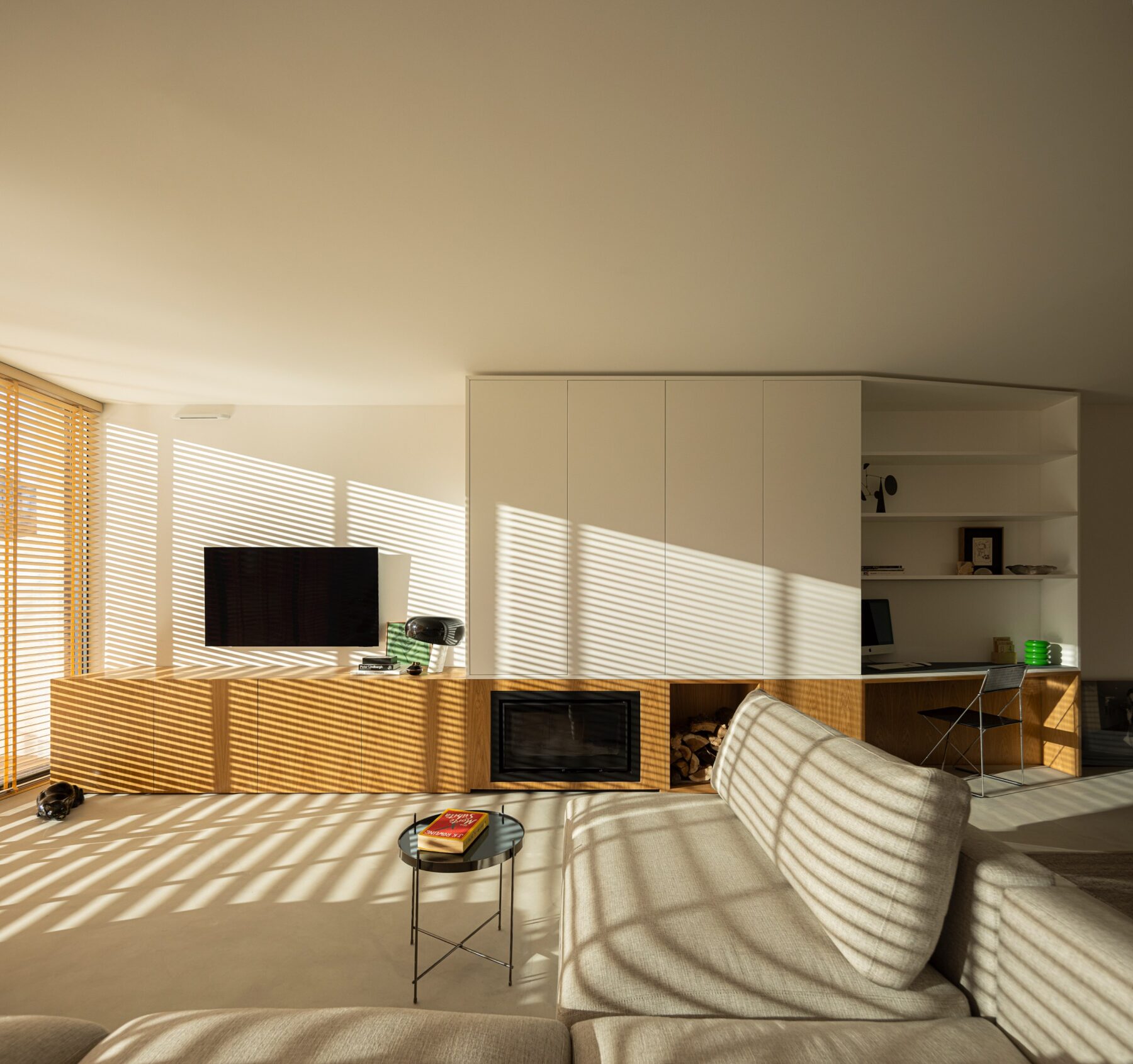 Sala de estar com luz natural filtrada por estores de madeira, sofá e móvel com lareira — Casa sem Rua