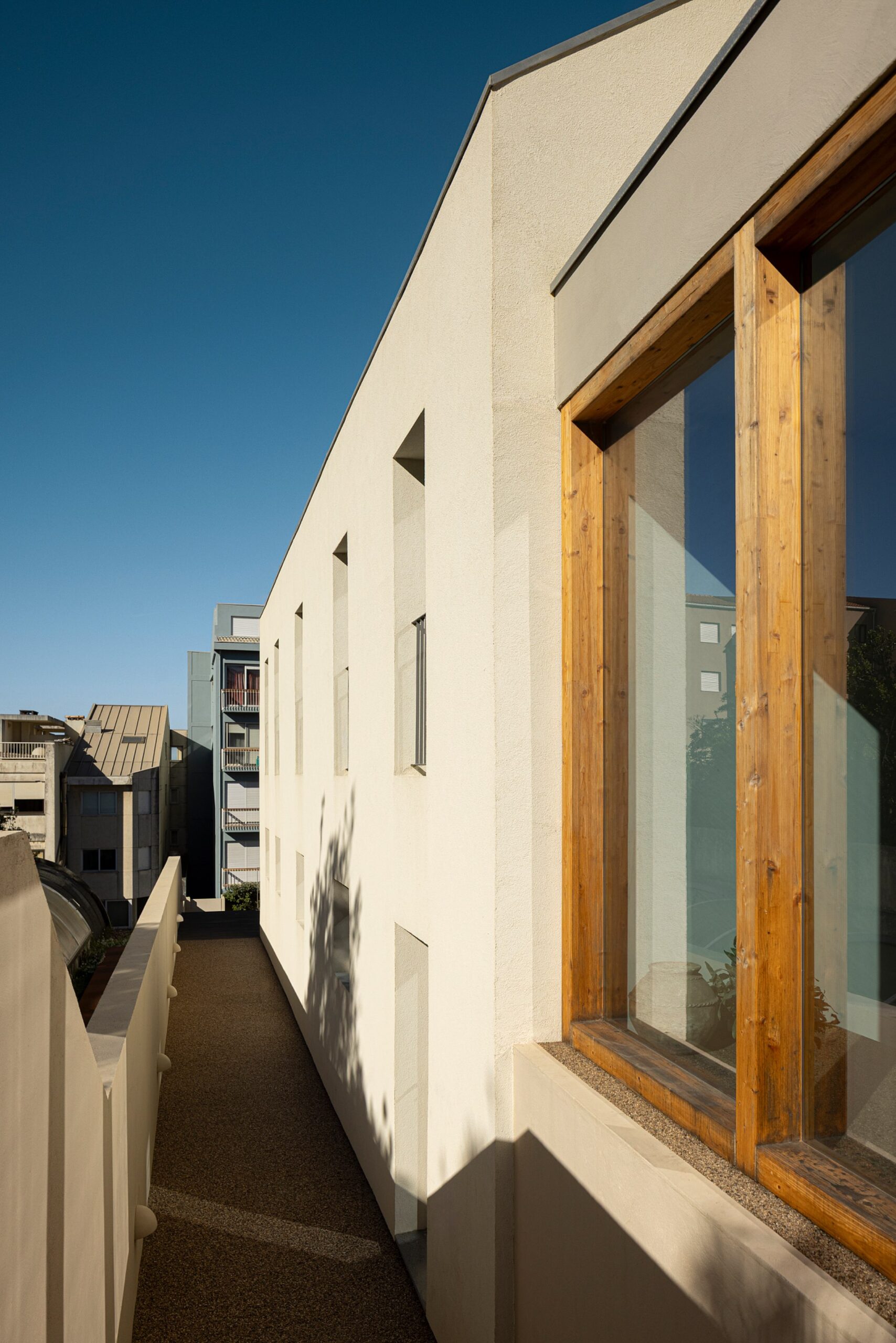 Fachada lateral com revestimento branco, vãos verticais e estrutura em madeira — Casa sem Rua
