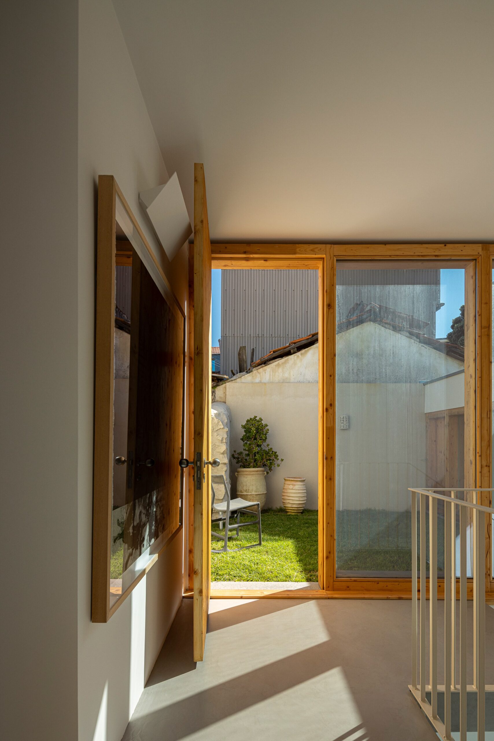 Interior com porta em madeira, vão envidraçado e vista para o jardim relvado — Casa sem Rua