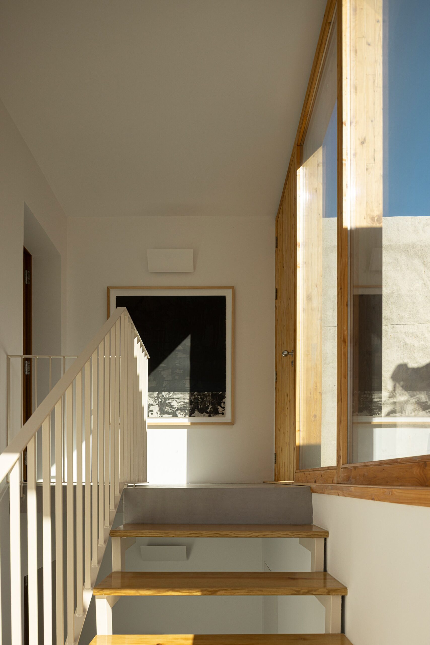 Escadaria interior com degraus em madeira, corrimão branco e vão envidraçado — Casa sem Rua