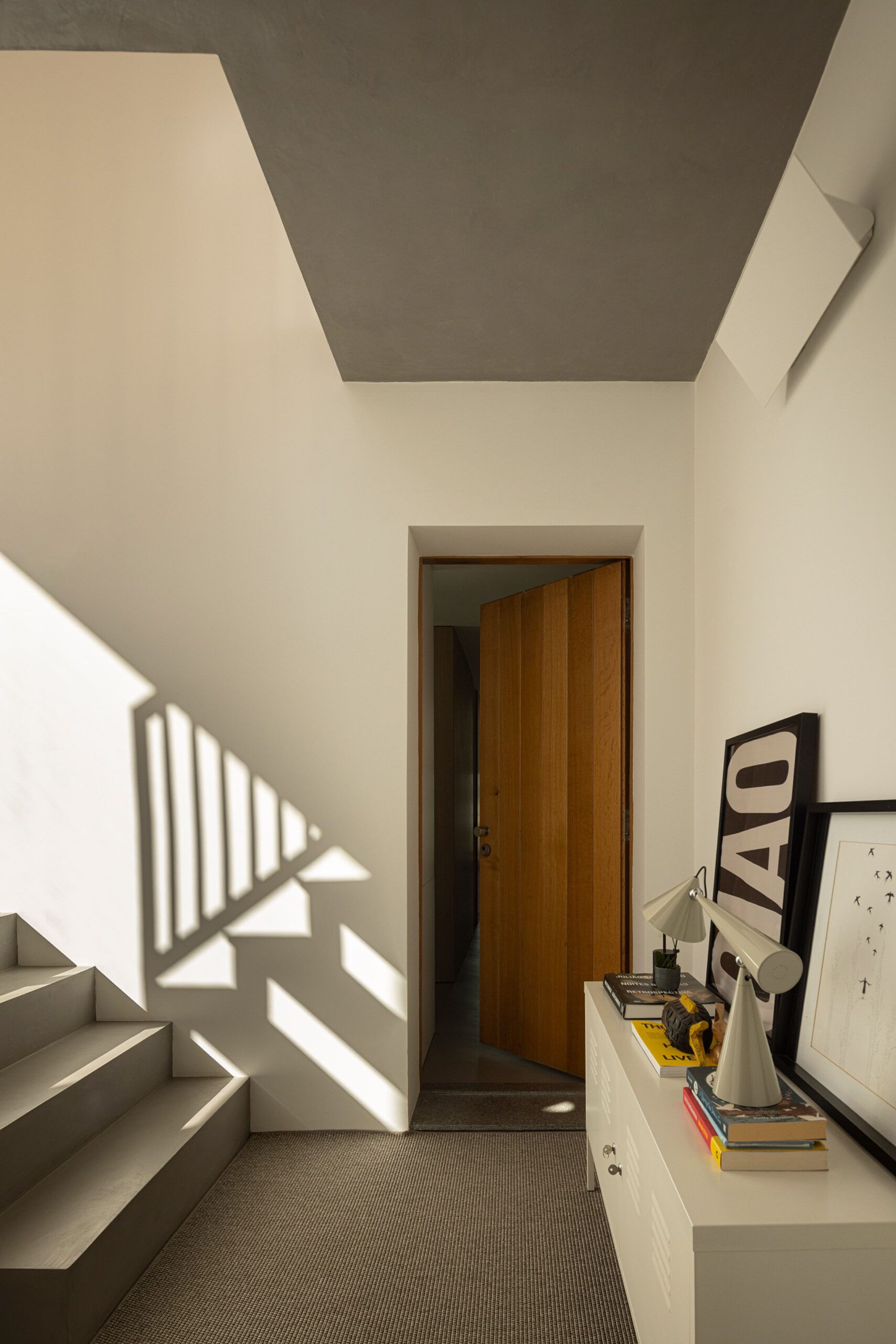 Hall de entrada com escadaria em betão, porta em madeira e candeeiro de teto — Casa sem Rua