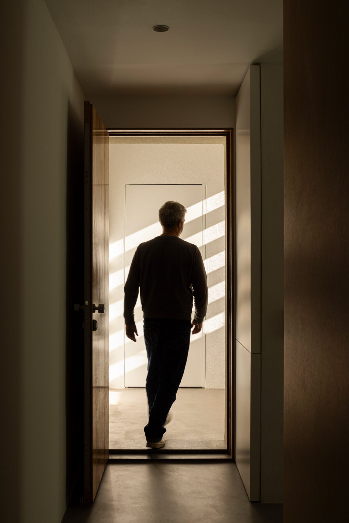 Corredor estreito com porta em madeira e luz natural a incidir no pavimento — Casa sem Rua