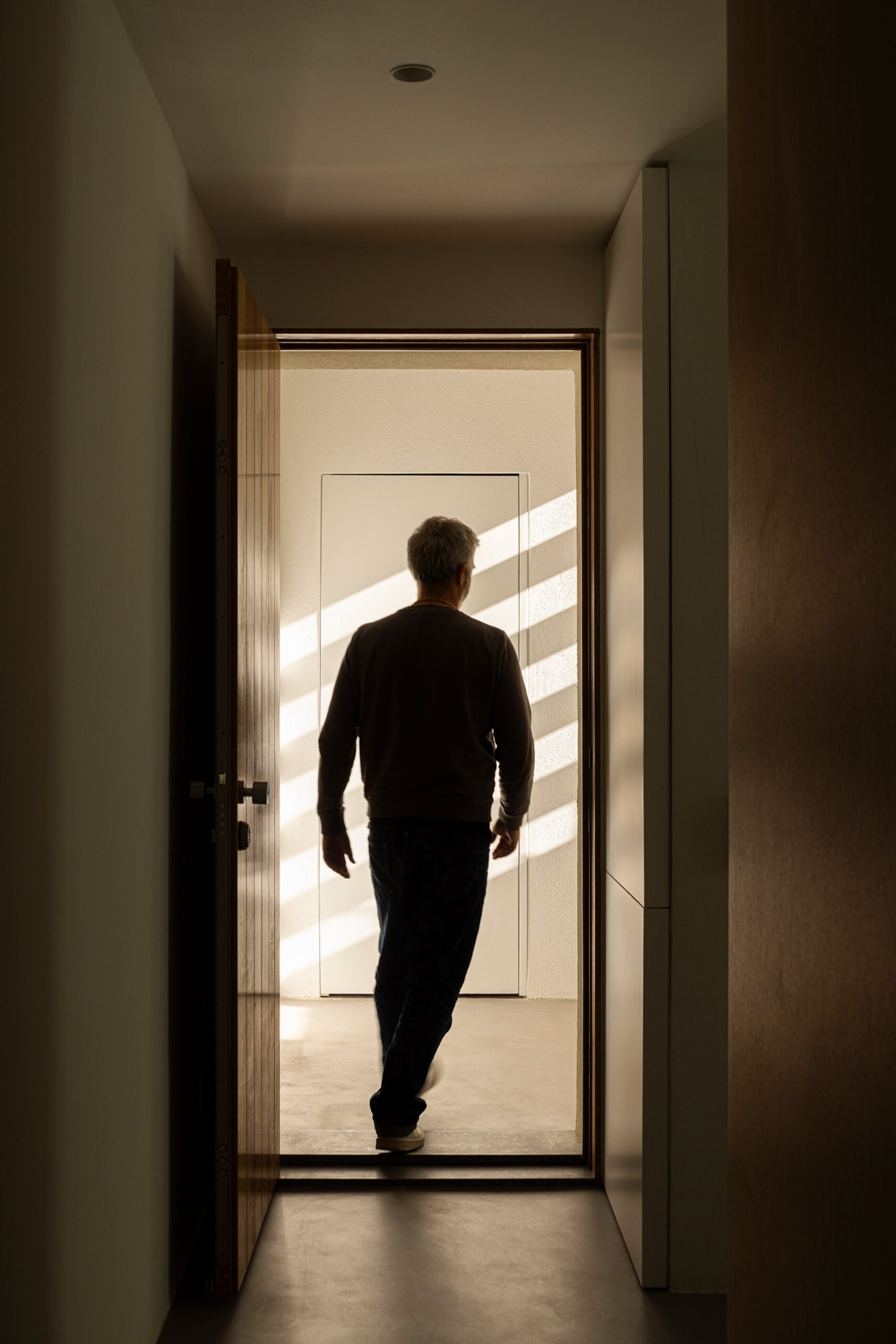 Corredor estreito com porta em madeira e luz natural a incidir no pavimento — Casa sem Rua