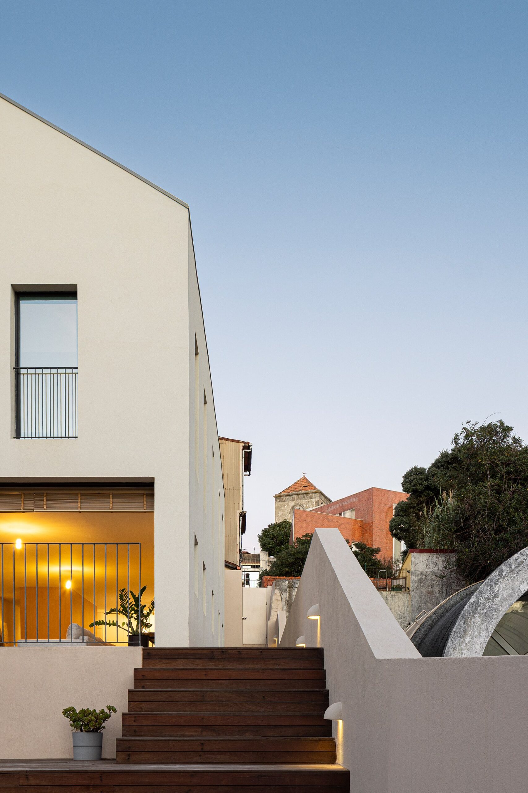 Fachada principal da moradia com revestimento branco, escadaria em madeira e luz artificial — Casa sem Rua