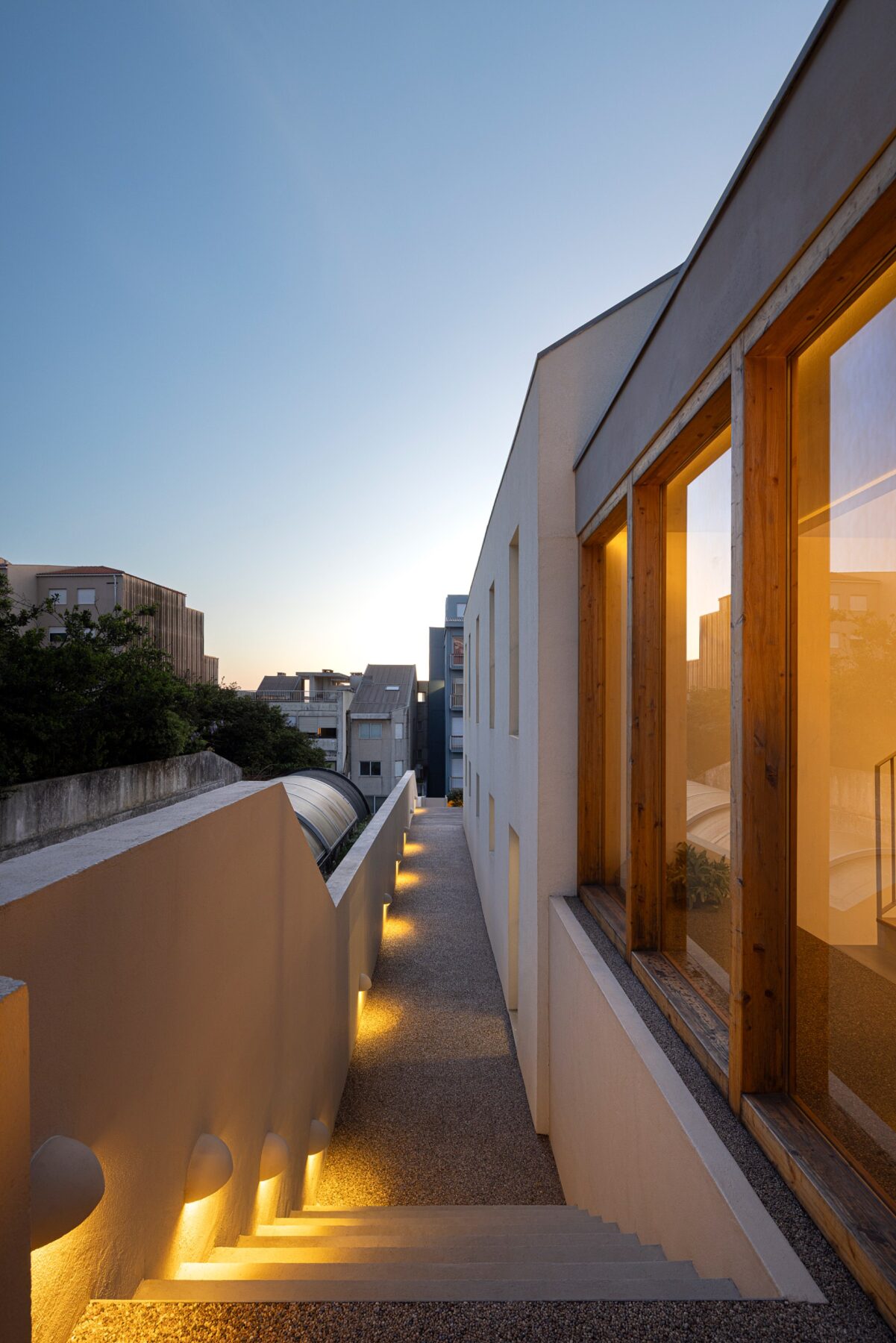 Corredor exterior com pavimento em gravilha, paredes brancas e iluminação embutida — Casa sem Rua
