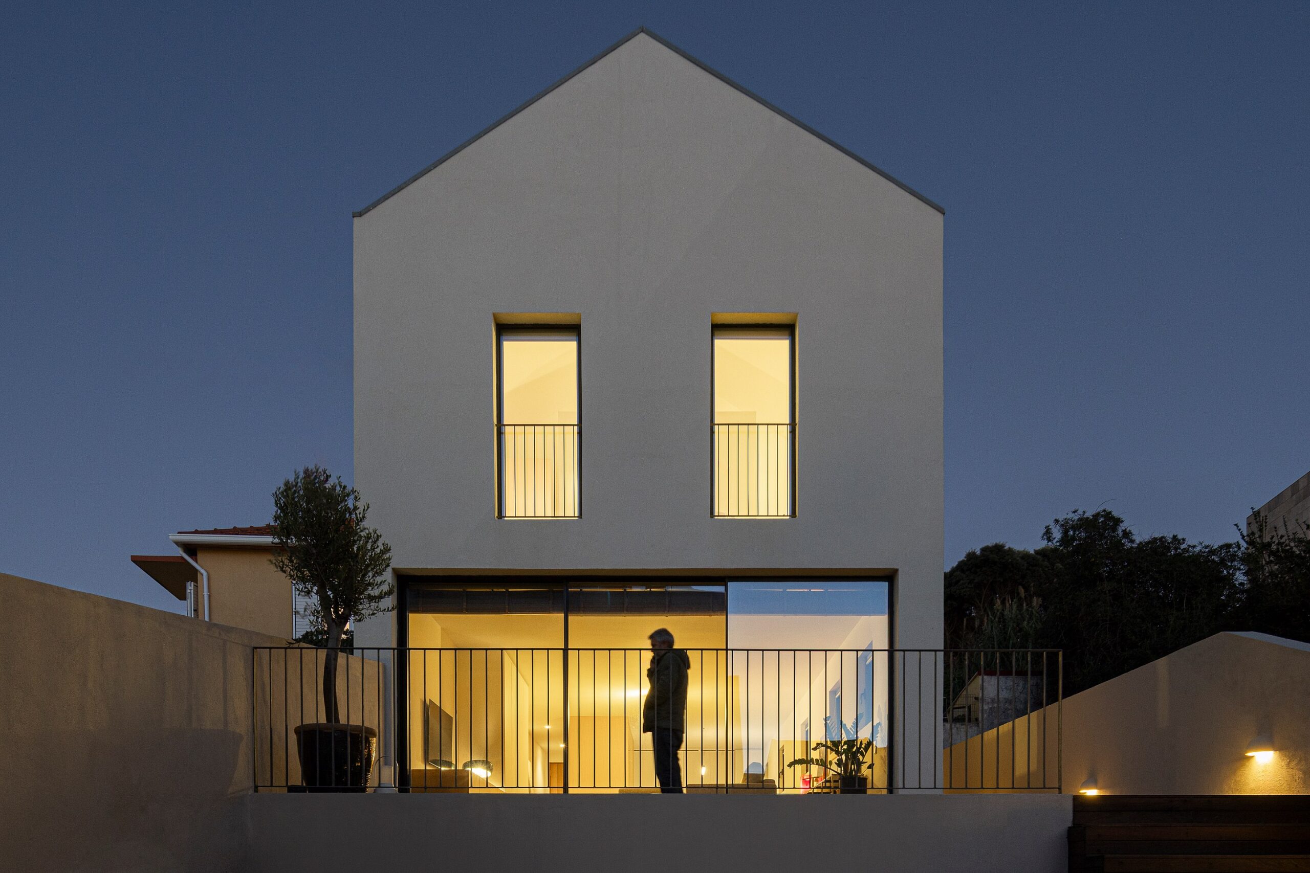 Fachada principal da moradia com revestimento branco, varanda e iluminação interior — Casa sem Rua