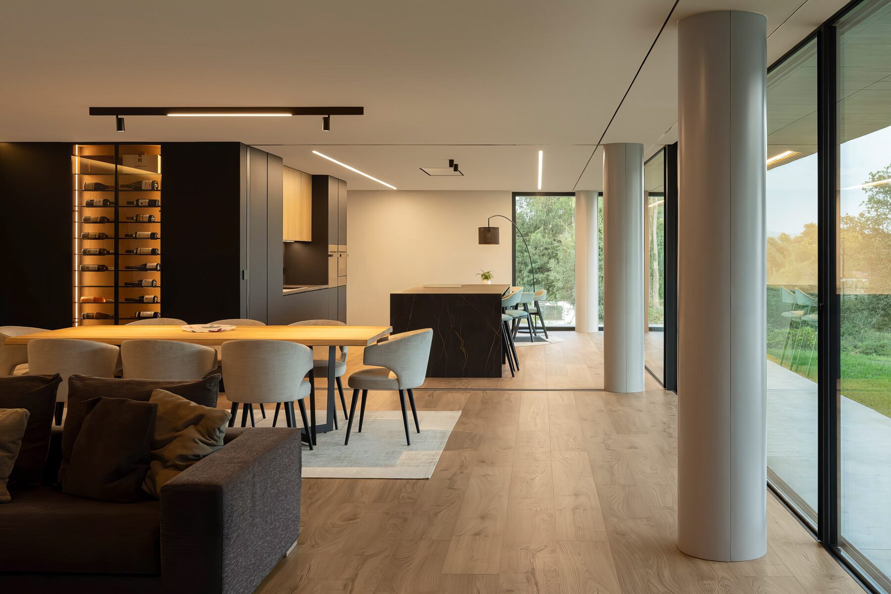 Sala de jantar e estar em open space, com pavimento em madeira, pilares cilíndricos e grandes vãos envidraçados — Quinta da Casa (Habitação QC)