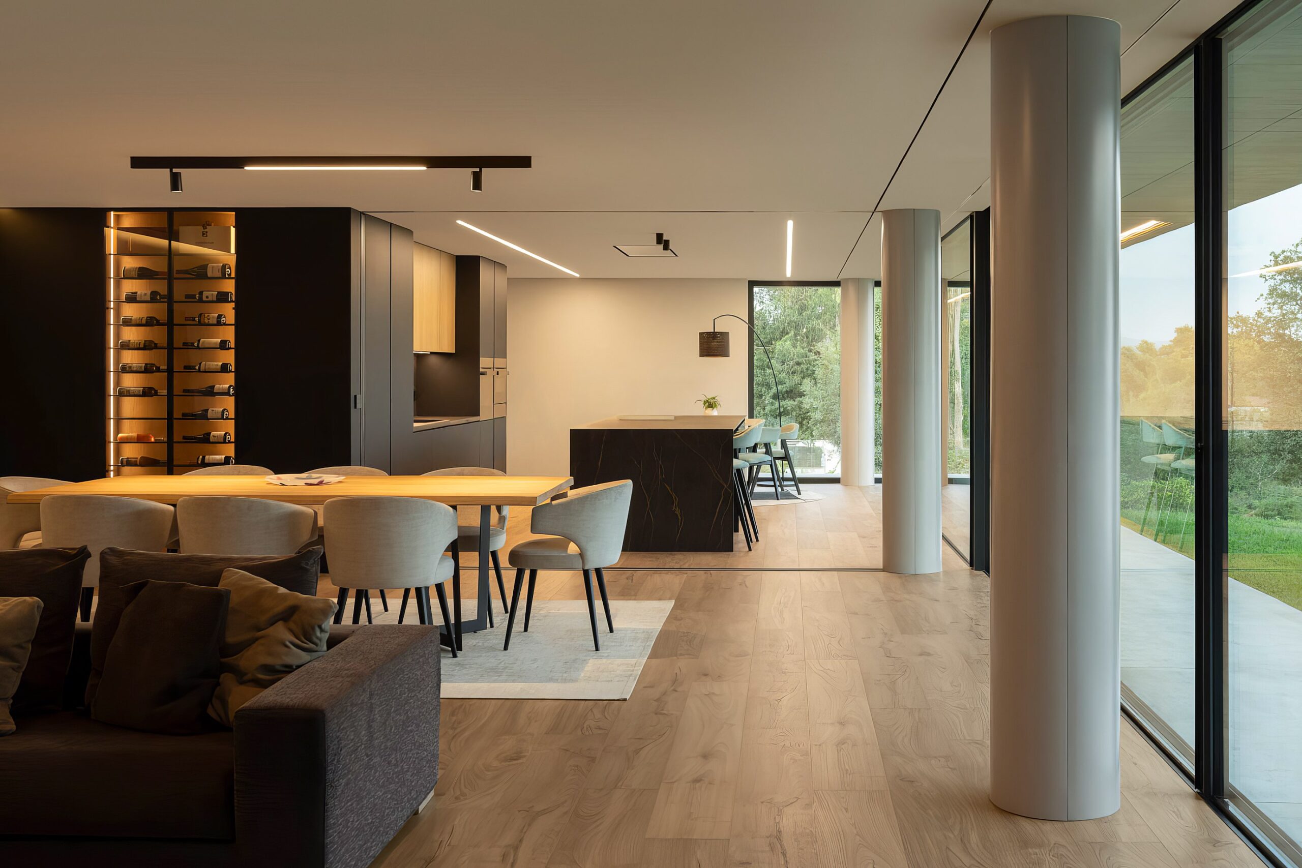 Sala de jantar e estar em open space, com pavimento em madeira, pilares cilíndricos e grandes vãos envidraçados — Quinta da Casa (Habitação QC)