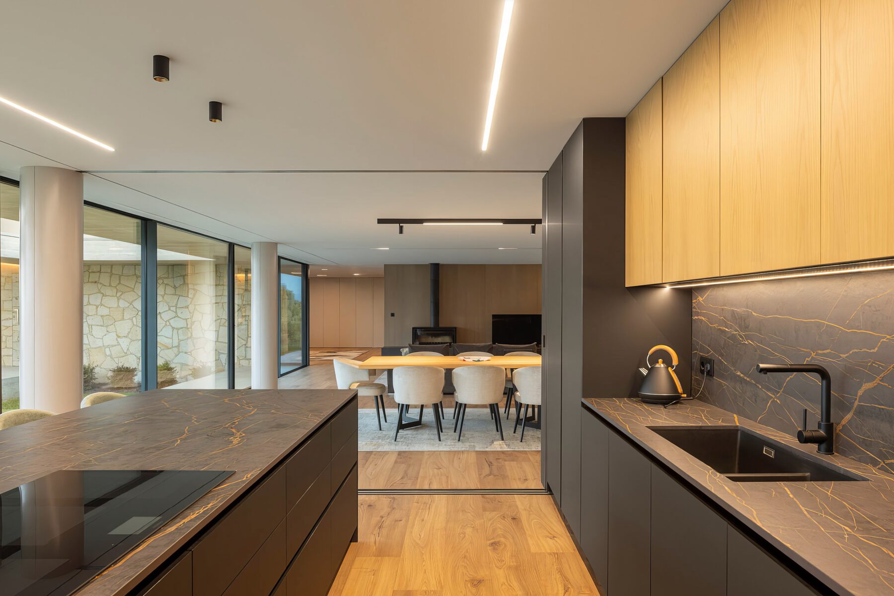 Cozinha e sala de jantar em open space, com pavimento em madeira, armários cinzentos e iluminação linear — Quinta da Casa (Habitação QC)