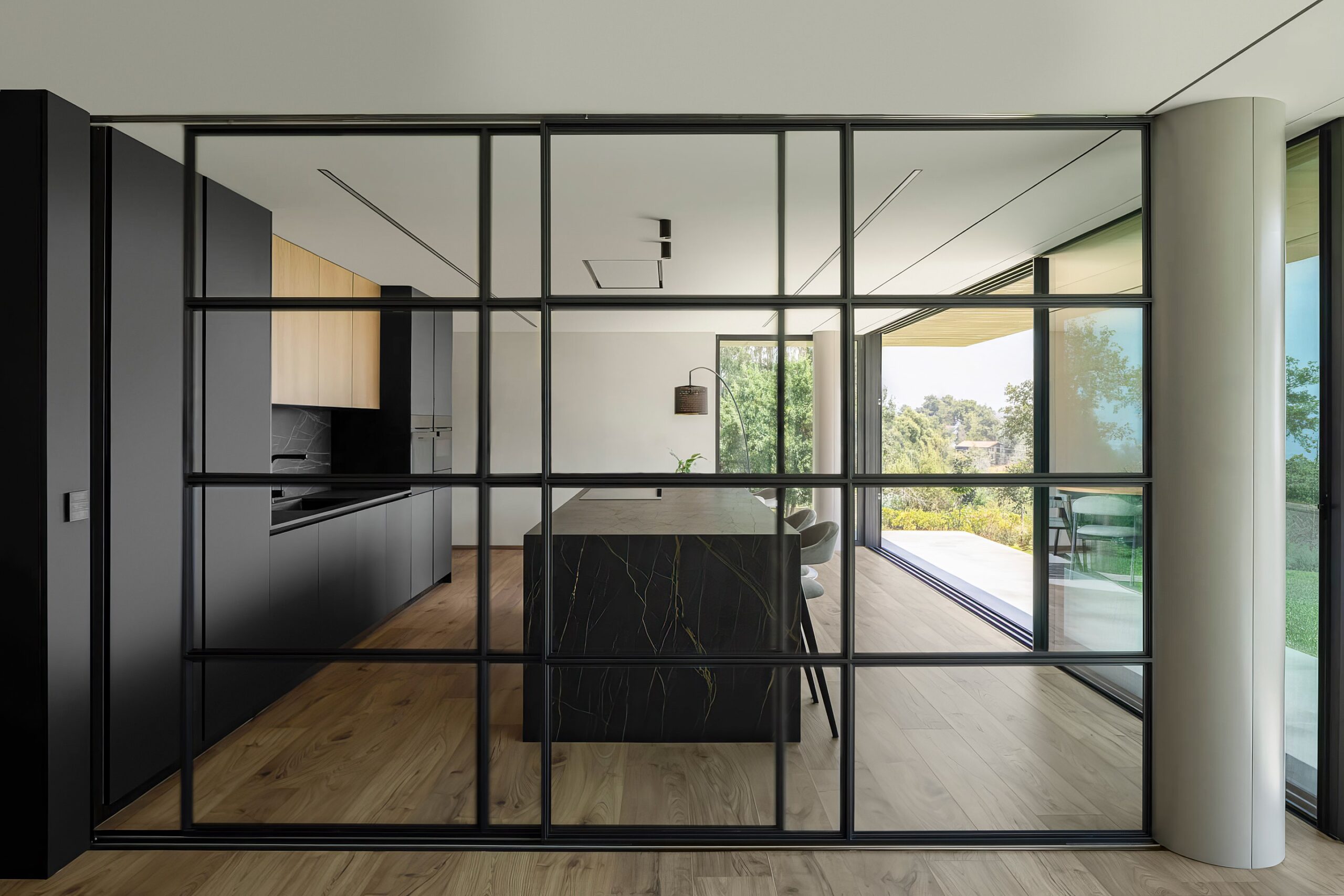 Cozinha com ilha em mármore negro, armários em madeira mel e cinzento escuro, pavimento em madeira e divisória envidraçada — Quinta da Casa (Habitação QC)