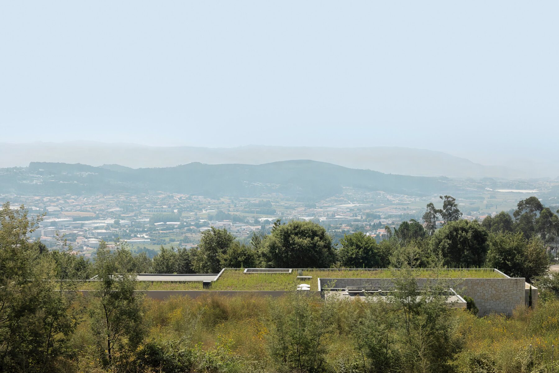 Moradia térrea com cobertura ajardinada, em betão aparente e alvenaria de granito, integrada na paisagem — Quinta da Casa (Habitação QC)