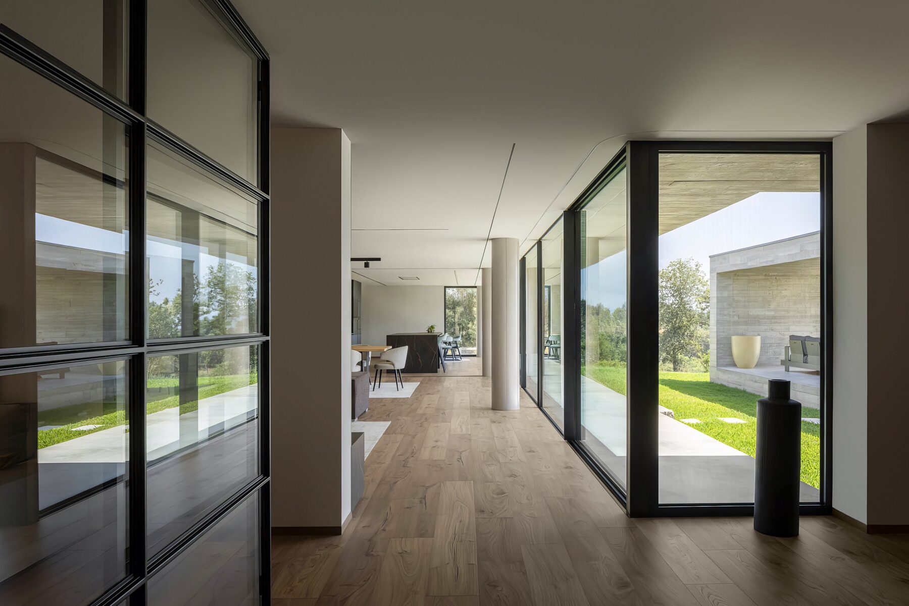 Corredor interior com pavimento em madeira, paredes brancas, vãos envidraçados e pilares cilíndricos — Quinta da Casa (Habitação QC)