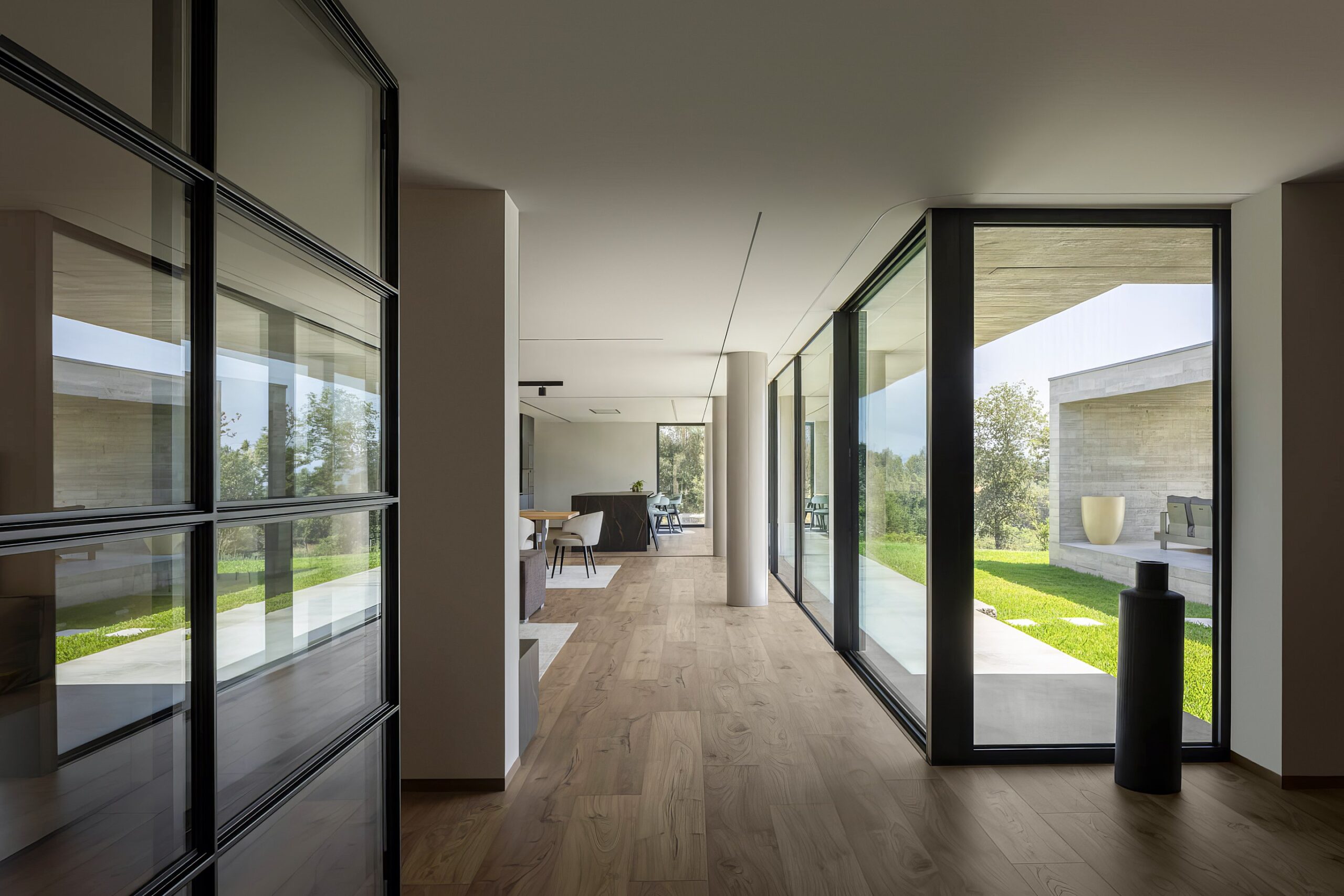 Corredor interior com pavimento em madeira, paredes brancas, vãos envidraçados e pilares cilíndricos — Quinta da Casa (Habitação QC)