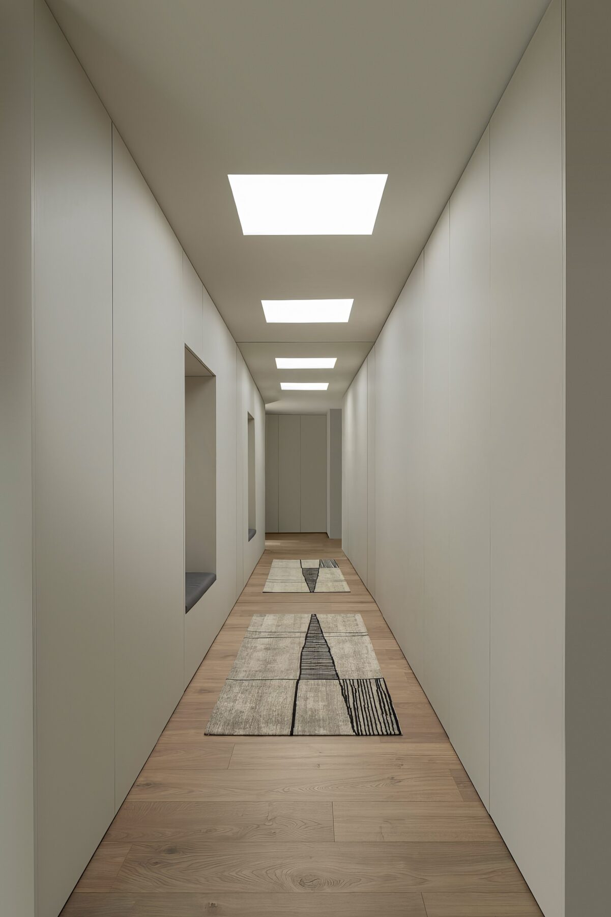 Corredor com pavimento em madeira, armários brancos e iluminação zenital, com tapetes geométricos — Quinta da Casa (Habitação QC)